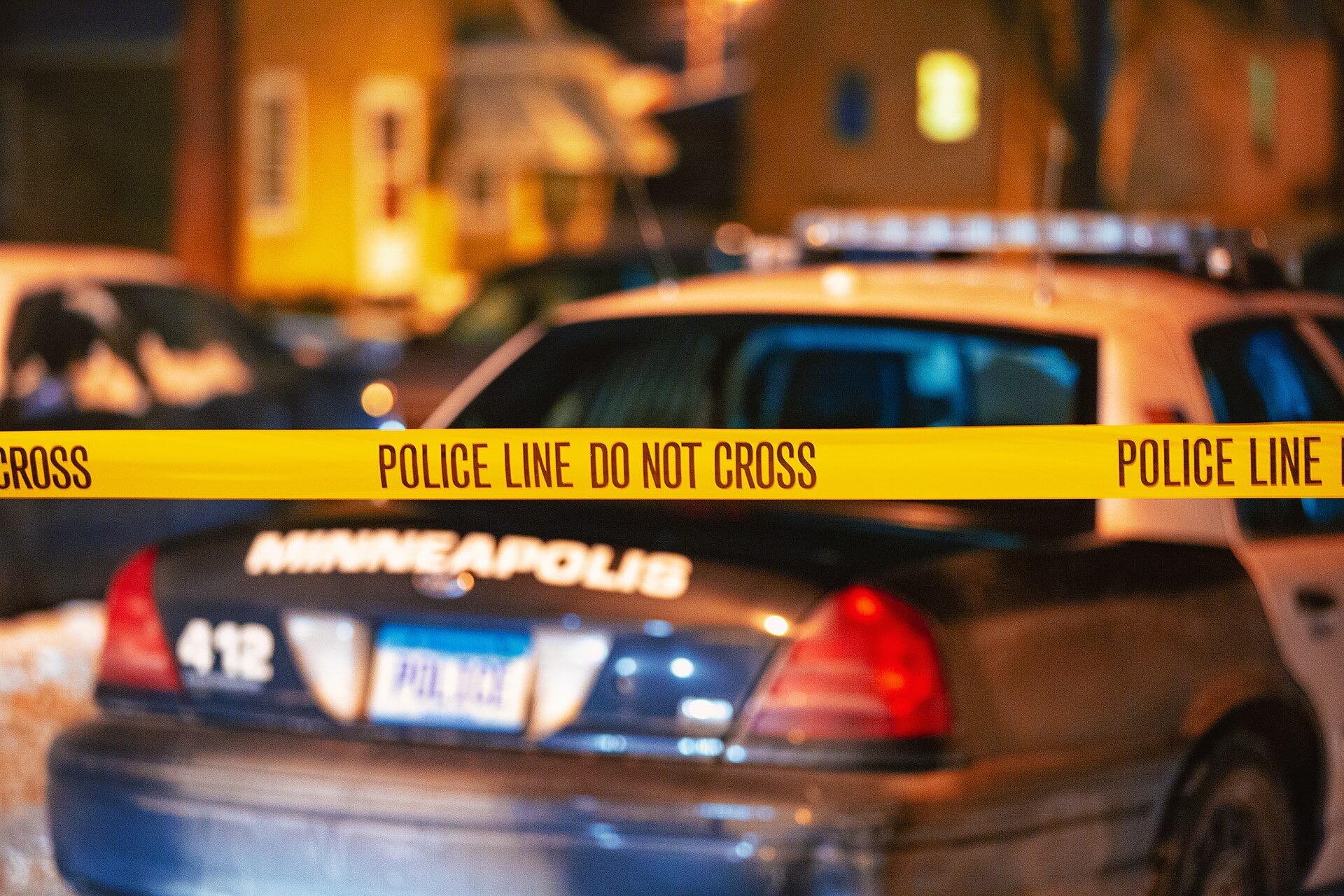 Police line tape stretched across a night crime scene in front of a patrol car